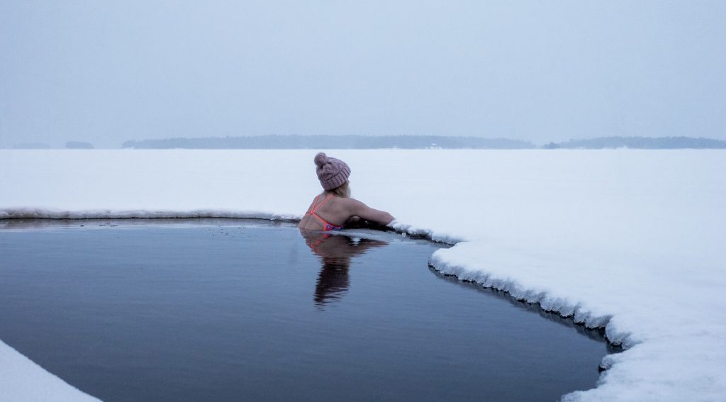 Una valiente mujer sumergida en las gélidas aguas de un lago helado, mostrando la importancia de los baños de hielo para la recuperación y rendimiento